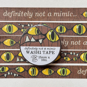 Image of a illustrated comic style washi tape design with a wood background and classic mimic eyes and teeth, and the words &quot;definitely not a mimic&quot; Also shows a packaged version with dimensions - 15 mm x 10 m