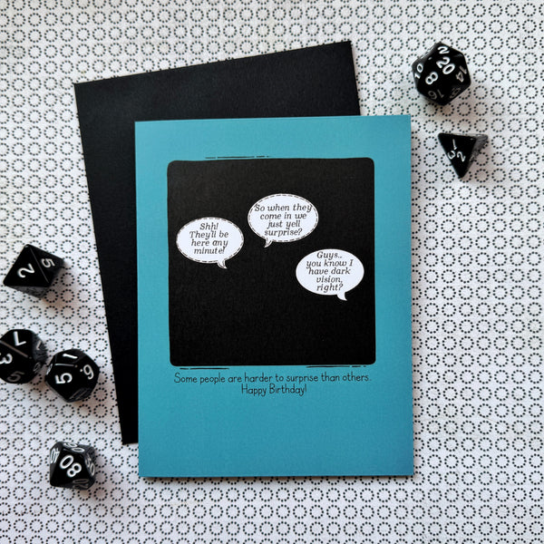 Picture shows a blue greeting card with a comic illustration - a black square with 3 speech bubbles. The first says "Shh! They'll be here any minute!" The second says "So they come in, we just yell surprise?" And the third says "Guys...you know I have dark vision, right?" The caption beneath the illustration reads "Some people are harder to surprise than others... Happy Birthday!"