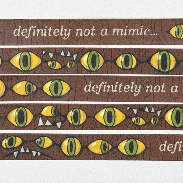 Image of a illustrated comic style washi tape design with a wood background and classic mimic eyes and teeth, and the words &quot;definitely not a mimic&quot;